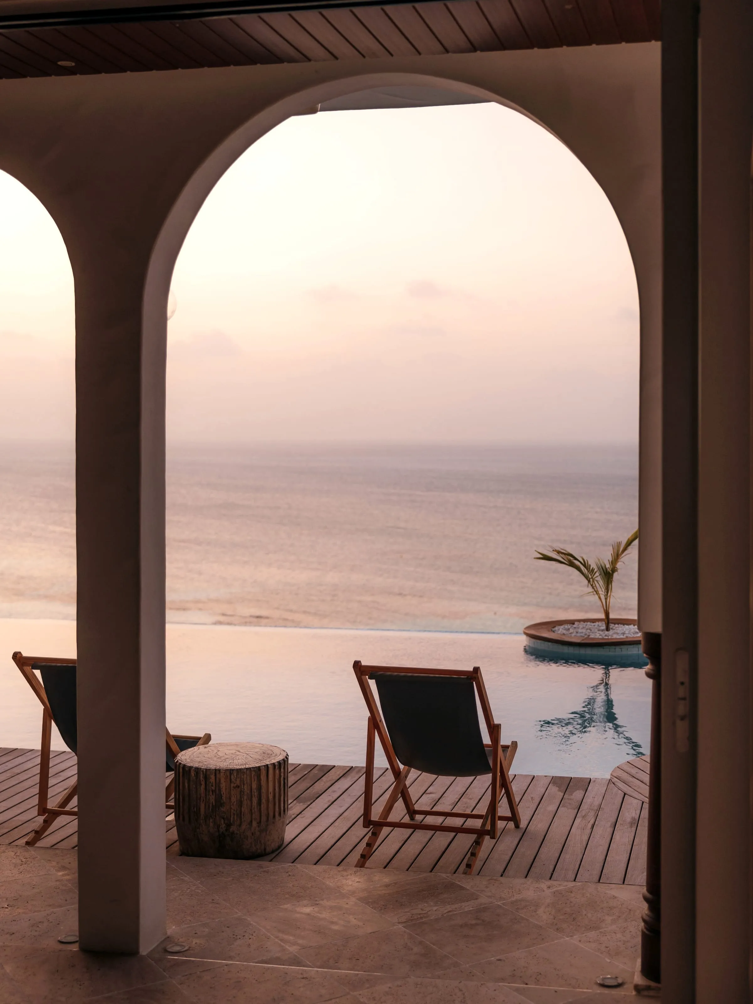 An archway framing the sea at sunset, chairs out on the deck