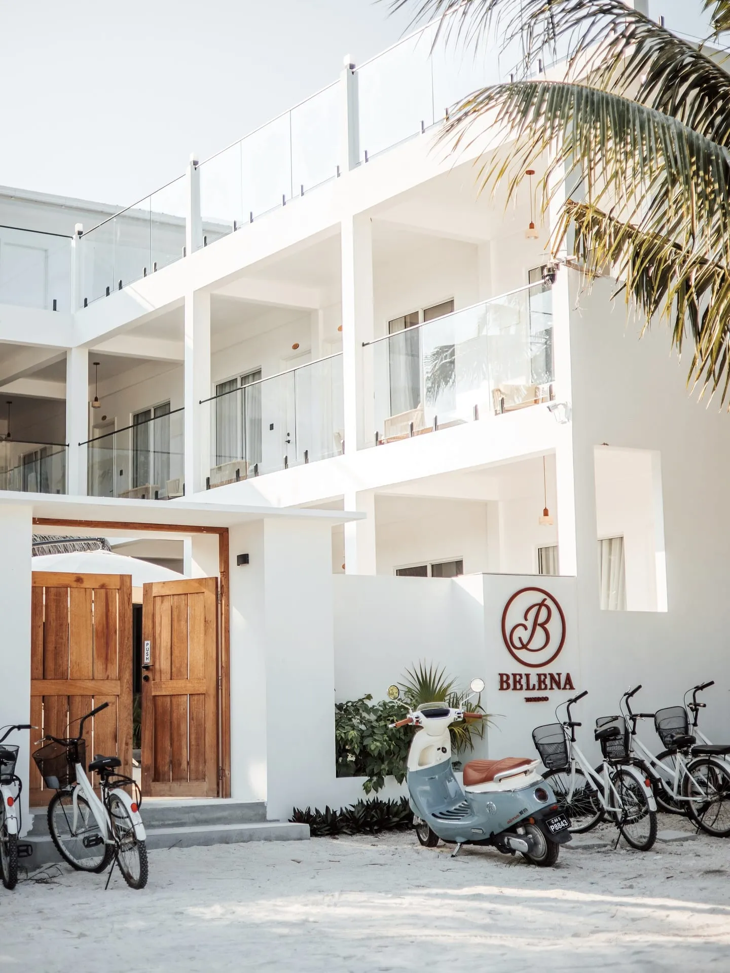 Bicycles and a scooter on the sand outside a white two-storey guesthouse