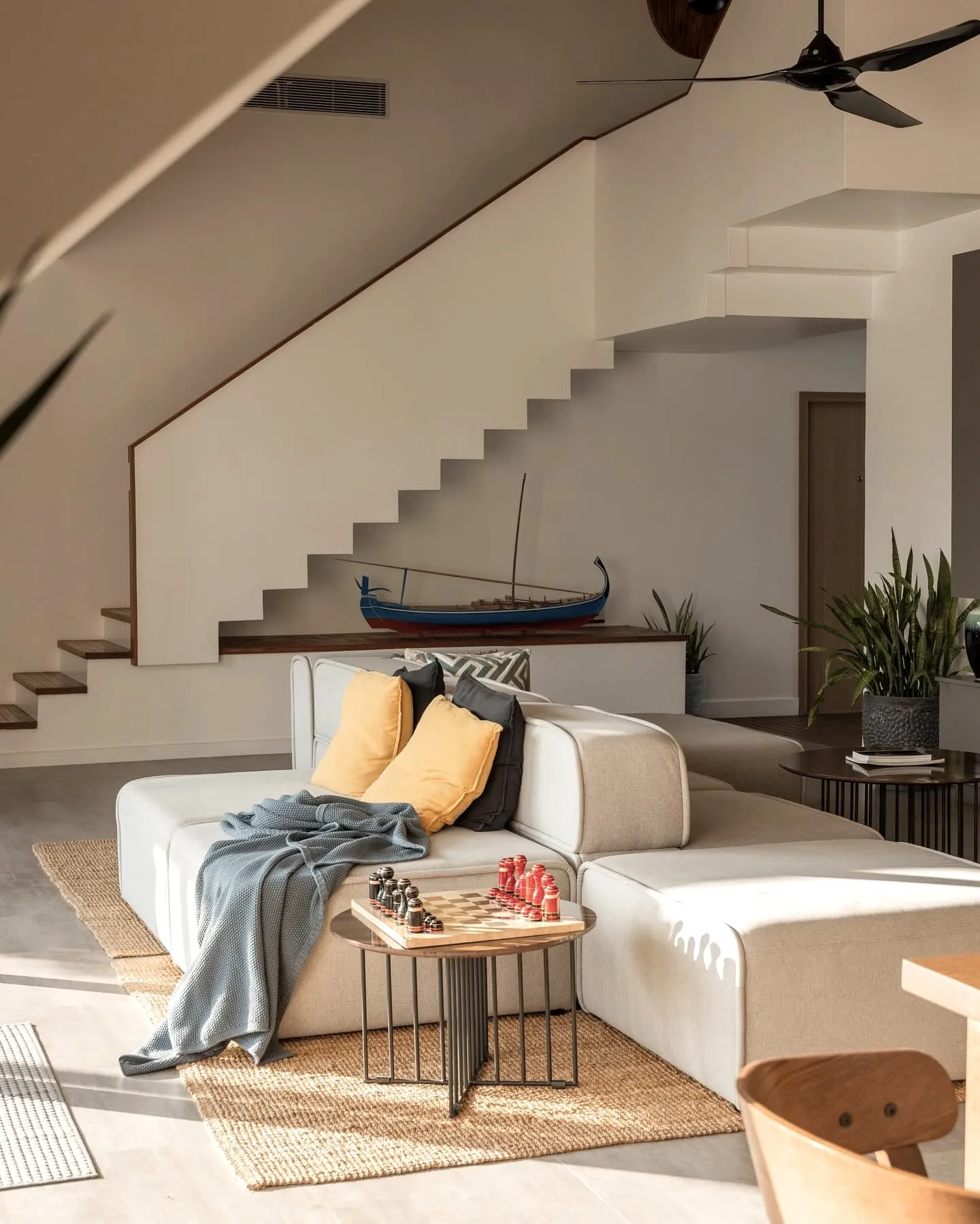 A low sofa beneath an open staircase, a model dhoni on the shelf behind