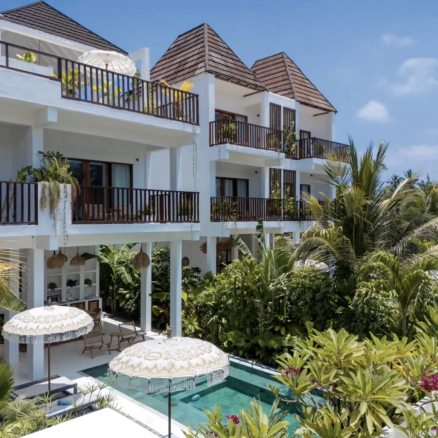 Woven parasols and a pool below cream balconies, set in greenery