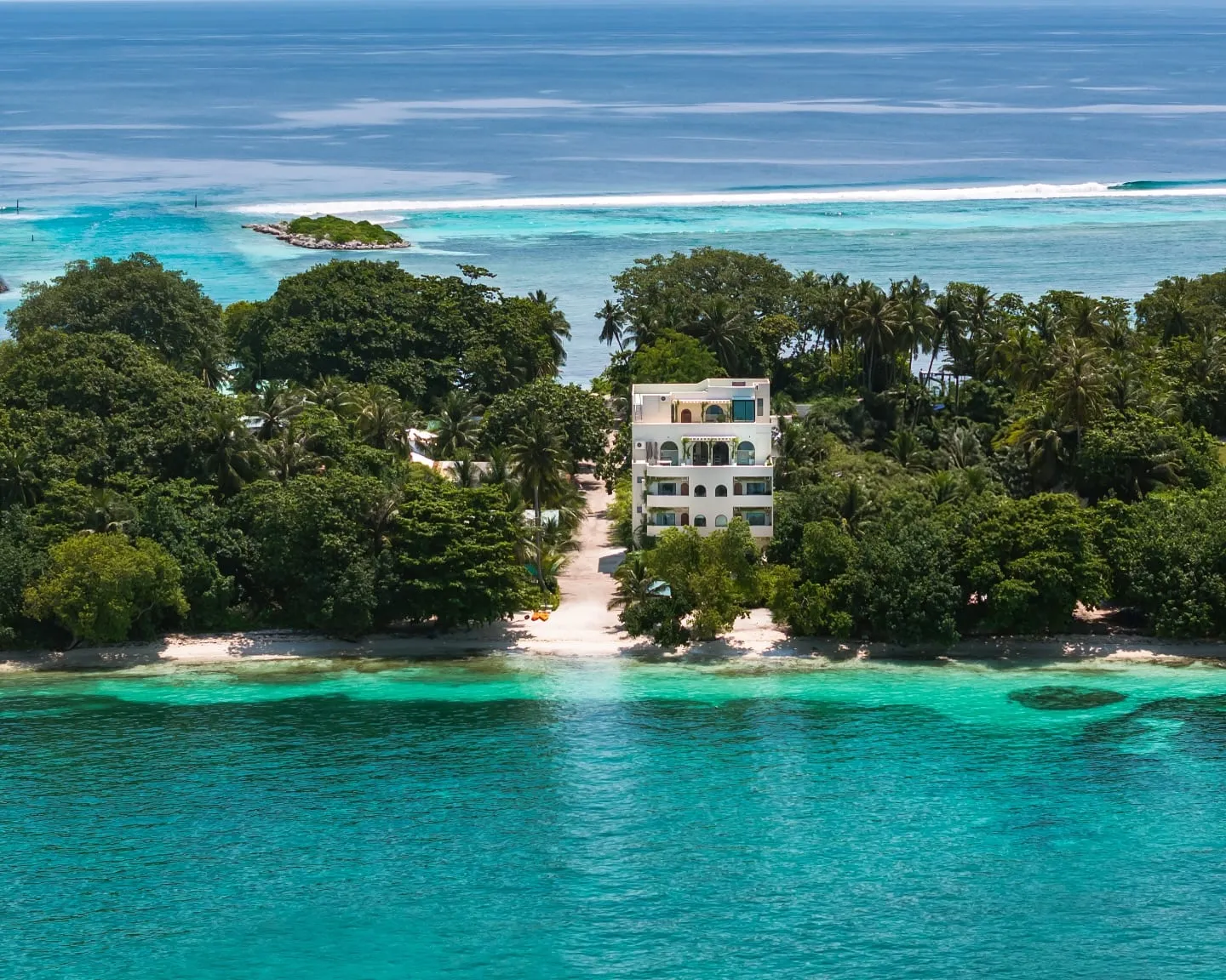 The house seen from the air, white against the trees, with the beach and reef in front of it